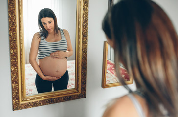 Pregnant woman looking her belly in the mirror