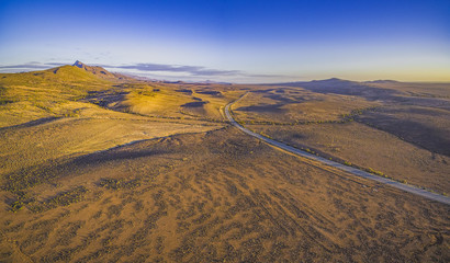 Rural road passing through dry land with scarce peaks at sunset - aerial panorama