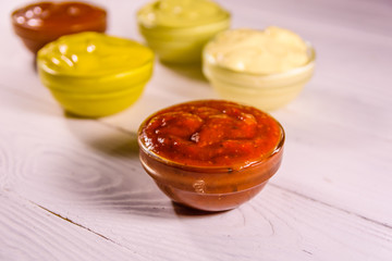 Different sauces in glass bowls on wooden table