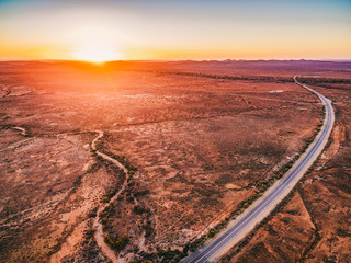 Oranje zonsondergang over droog land en landelijke snelweg die door Zuid-Australië slingert