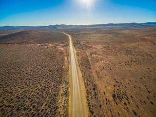 Rural road passing through dry land with scarce vegetation on bright sunny day - aerial view