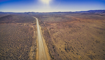 Rural road passing through dry land with scarce vegetation on bright sunny day - aerial panorama