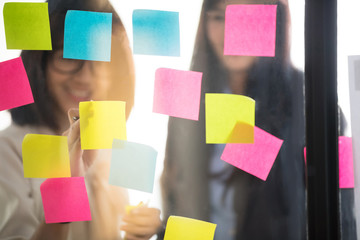 Creative businesspeople putting their ideas at sticky notes on window during a presentation in meeting room. Smiling partners brainstorm concept. Setup studio shooting.