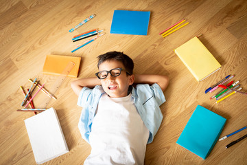 Cute happy preschool boy with eye glasses on smiling laughing, lying  on the floor, colorful books...
