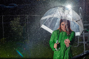 Smiling young woman in the green coat in the rain with a transparent umbrella in the night. ...