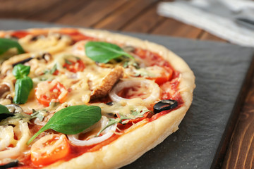 Slate plate with tasty pizza on wooden table, closeup