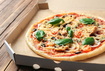 Tasty pizza in cardboard box on wooden table, closeup