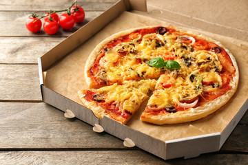 Tasty pizza in cardboard box on wooden table