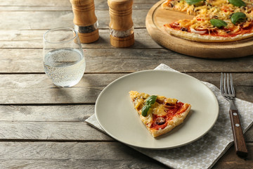 Plate with slice of tasty pizza on wooden table