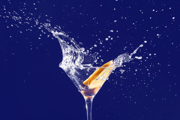 Glass with splashing cocktail and slice of orange on black background