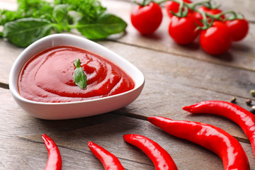 Bowl of delicious tomato sauce with chili peppers on wooden table