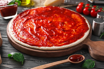 Pizza dough with tasty tomato sauce on wooden table