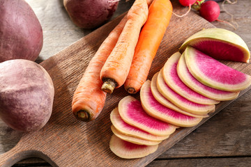 Wooden board with radish and carrots on table