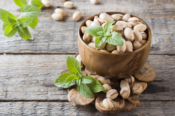 Delicious salted pistachios and fresh mint leaves on wooden background.