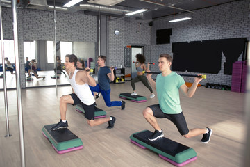 Group of young people working out with dumbbells and steppers in gym