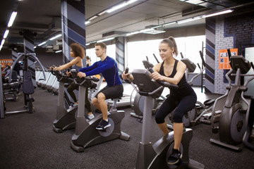 Young people doing exercises on elliptical trainer in gym