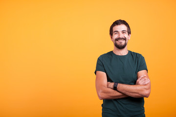 Handsome man with his arms crossed smiling at the camera isolated on yellow background. Portrait of attractive bearded confident person in studio photo - obrazy, fototapety, plakaty