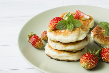 Curd pancakes with strawberries and mint on a plate.