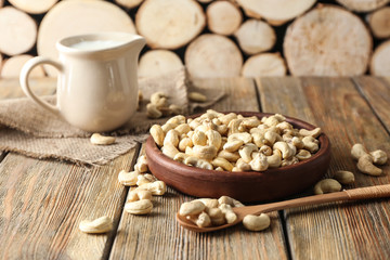 Plate with tasty cashew nuts and jug of milk on wooden table