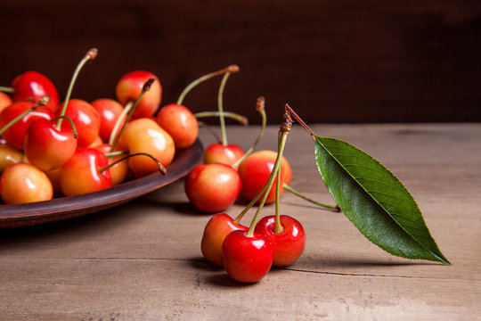 Clay plate with yellow sweet cherry on wooden background.