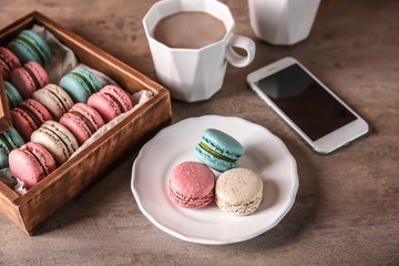 Plate with tasty macarons and cups of coffee on table