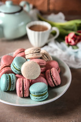 Plate with tasty macarons and coffee set on table