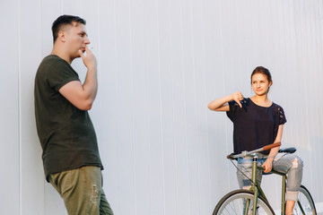 Fashionable attractive guy showing a middle finger, fuck sign to a cute pretty girl on bike, while she is showing thumb down on his gesture. Outdoors.