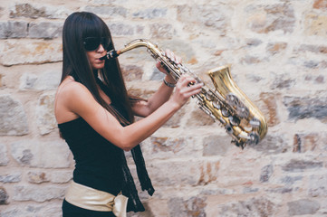 Young brunette girl having fun playing sax outdoor in a urban scene