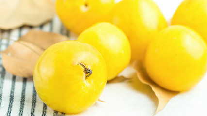 Bunch of ripe juicy organic yellow plums dry orange autumn leaves on white cotton towel. Autumn fall Produce. Vivid Colors. Provence rural kitchen interior. Cozy atmosphere