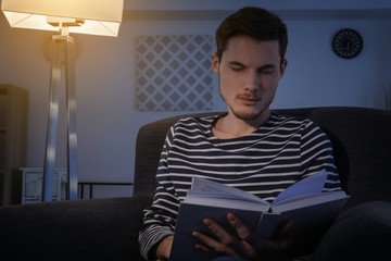 Fototapeta premium Young man reading book in evening at home