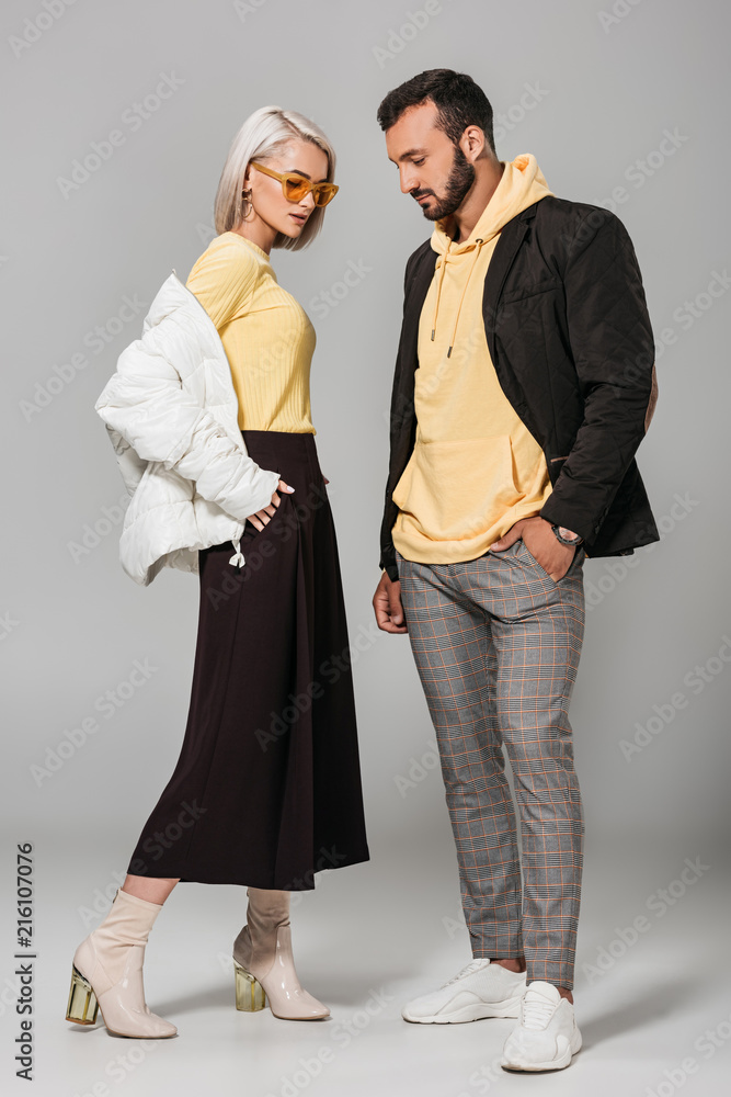 Wall mural stylish young man and woman in autumn outfits posing on grey background