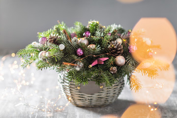 Christmas or New Year greeting card with a wicker basket with pine cones, fir branches, decorative balls on old wooden background. Vintage style, selective focus. on the background lights garland