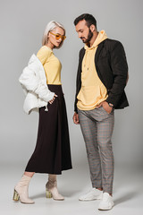 stylish young man and woman in autumn outfits posing on grey background