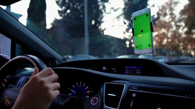 Close up shot of green screen cell phone mounted on windshield while caucasian woman drives the car and makes a right turn.