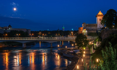 Night panorama of the Narva castle with the tower High Herman, Narva, Estonia. In the foreground is the city promenade and a bridge across the Narova River. The bridge connects Estonia and Russia