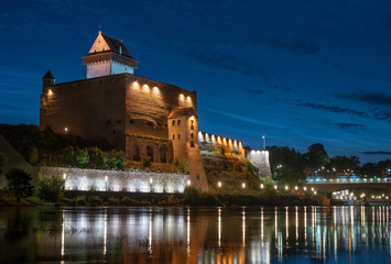 Fototapeta na wymiar Night view of Narva castle with the tower of High Herman, Narva, Estonia. The castle has a beautiful backlight. The castle is reflected in the water of the Narova River