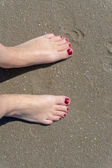 Naked feet with red nail polish in the sand on the beach