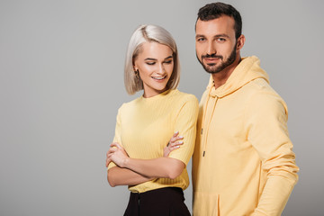 smiling woman with crossed arms posing in yellow clothes with boyfriend isolated on grey