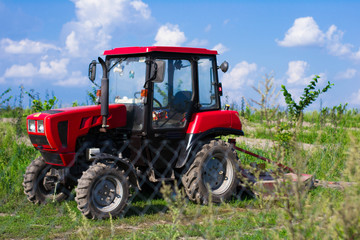 Modern red tractor on the agricultural field on sunny summer day.