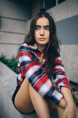 Fototapeta premium Girl wearing red plaid shirt and black shorts sitting on the parapet