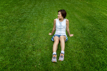 Asian woman wearing sportwear sitting on grass field with smile face and relaxed posture