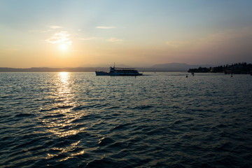 Fototapeta na wymiar Ferry floating on Lago di Garda near Scaliger Castle during beautiful sunset, Sirmione, Italy