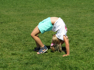 A little girl doing a yoga backbend (wheel pose) on a green grass. Stretching and fitness training...