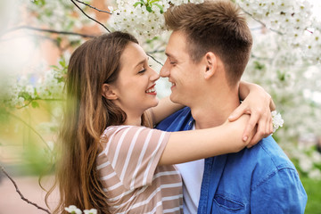 Happy young couple near blossoming tree in park on spring day