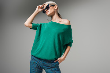 beautiful female model in sunglasses and green sweater posing isolated on grey background