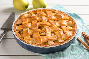 Dish with delicious apple pie on wooden background