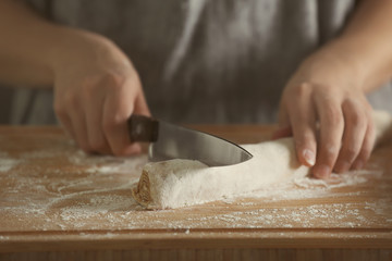 Woman cutting dough for cinnamon rolls on wooden board