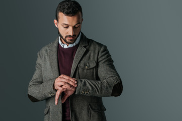 handsome man in tweed jacket looking at wristwatch, isolated on grey