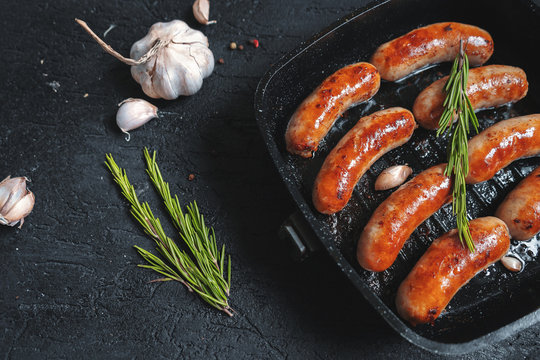 Top view on fried sausages in a black frying pan on a black stone table