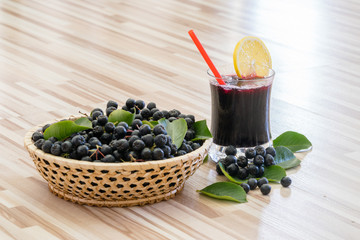 Fresh juice of chokeberry or Aronia melanocarpa with ice and lemon in glass and berry in basket near on wooden background